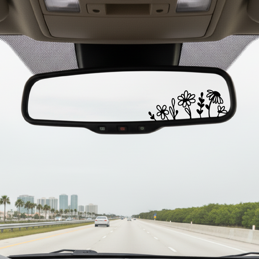 Car interior with a rearview mirror featuring floral decals on a highway.