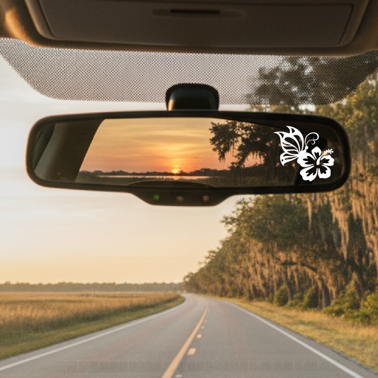 Car interior with a rearview mirror reflecting a sunset over a road flanked by trees.