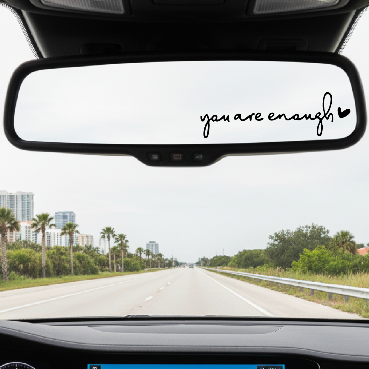 Car interior with a rearview mirror sticker reading 'you are enough' on a road trip.
