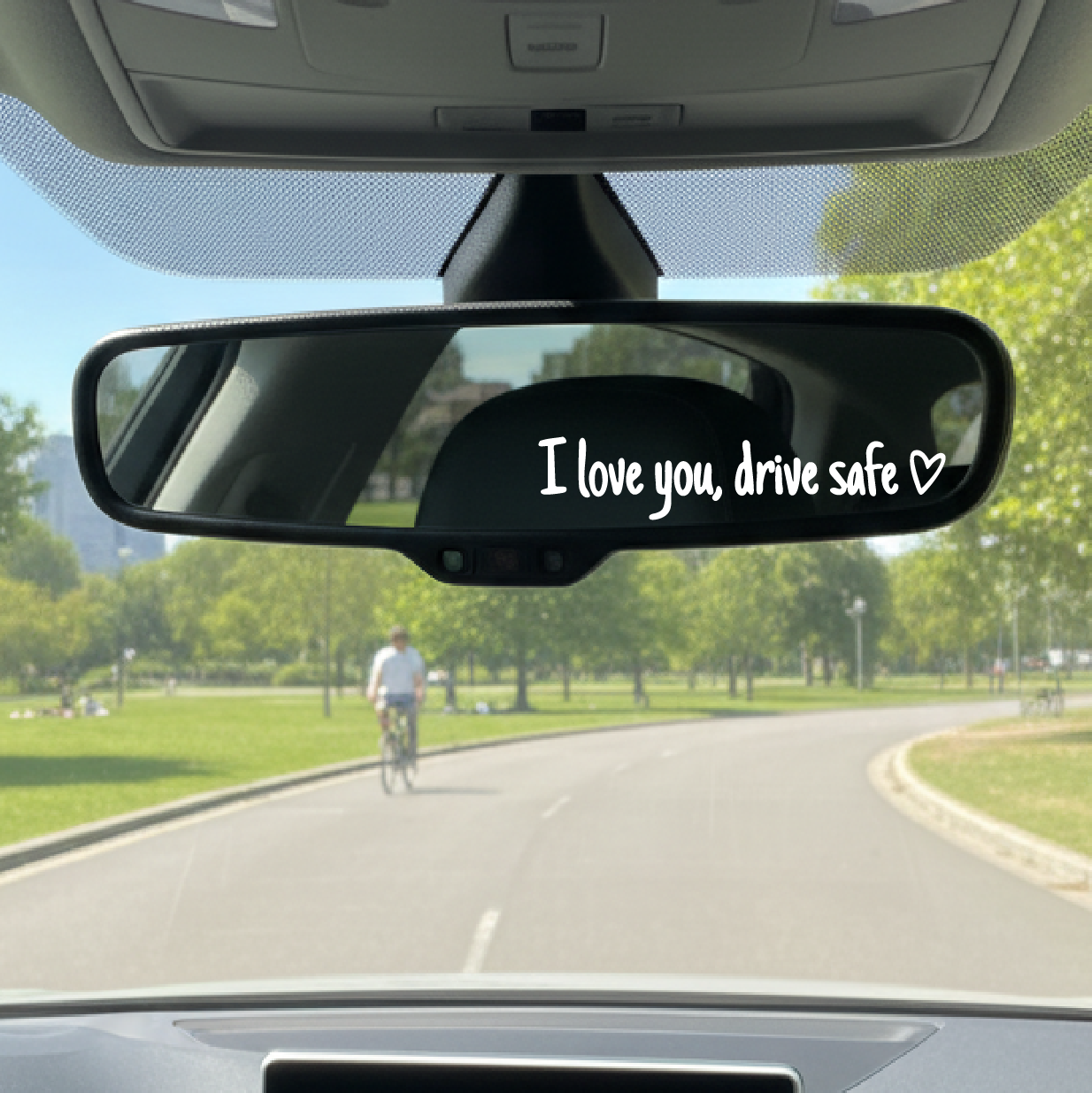 Car interior with a rearview mirror sticker reading 'I love you, drive safe' on a sunny day.