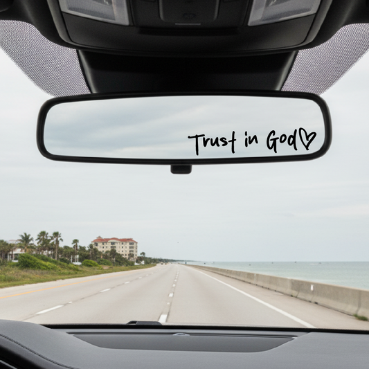 Car interior with 'Trust in God' decal on the rearview mirror, road ahead with scenic view.