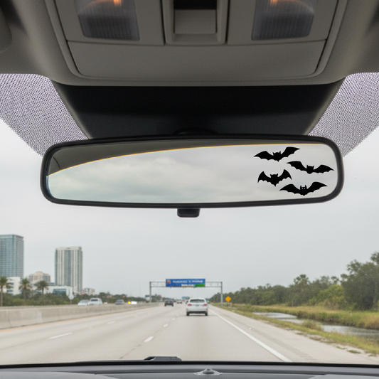 Car interior with a rearview mirror featuring bat decals on a highway.