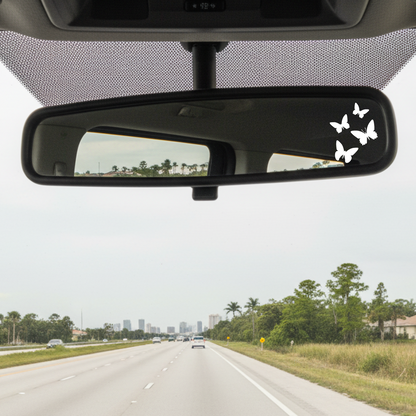 Car interior with a rearview mirror featuring butterfly decals on a road trip.