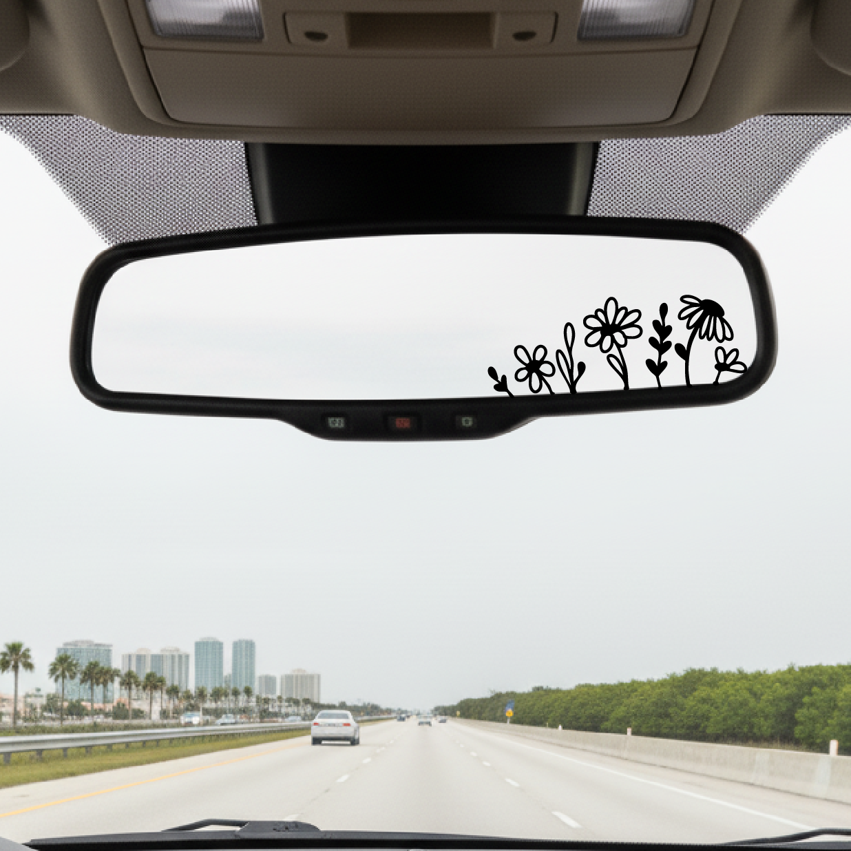 Car interior with a rearview mirror featuring floral decals on a highway.