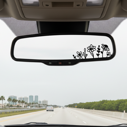 Car interior with a rearview mirror featuring floral decals on a highway.